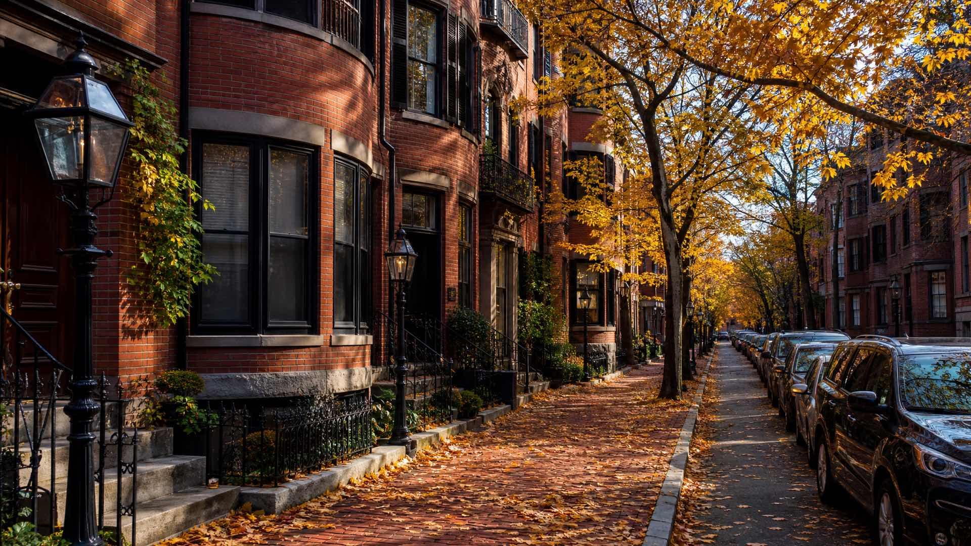 A narrow Boston street of red brick rowhouses with bow windows and iron railings under low autumn sunlight