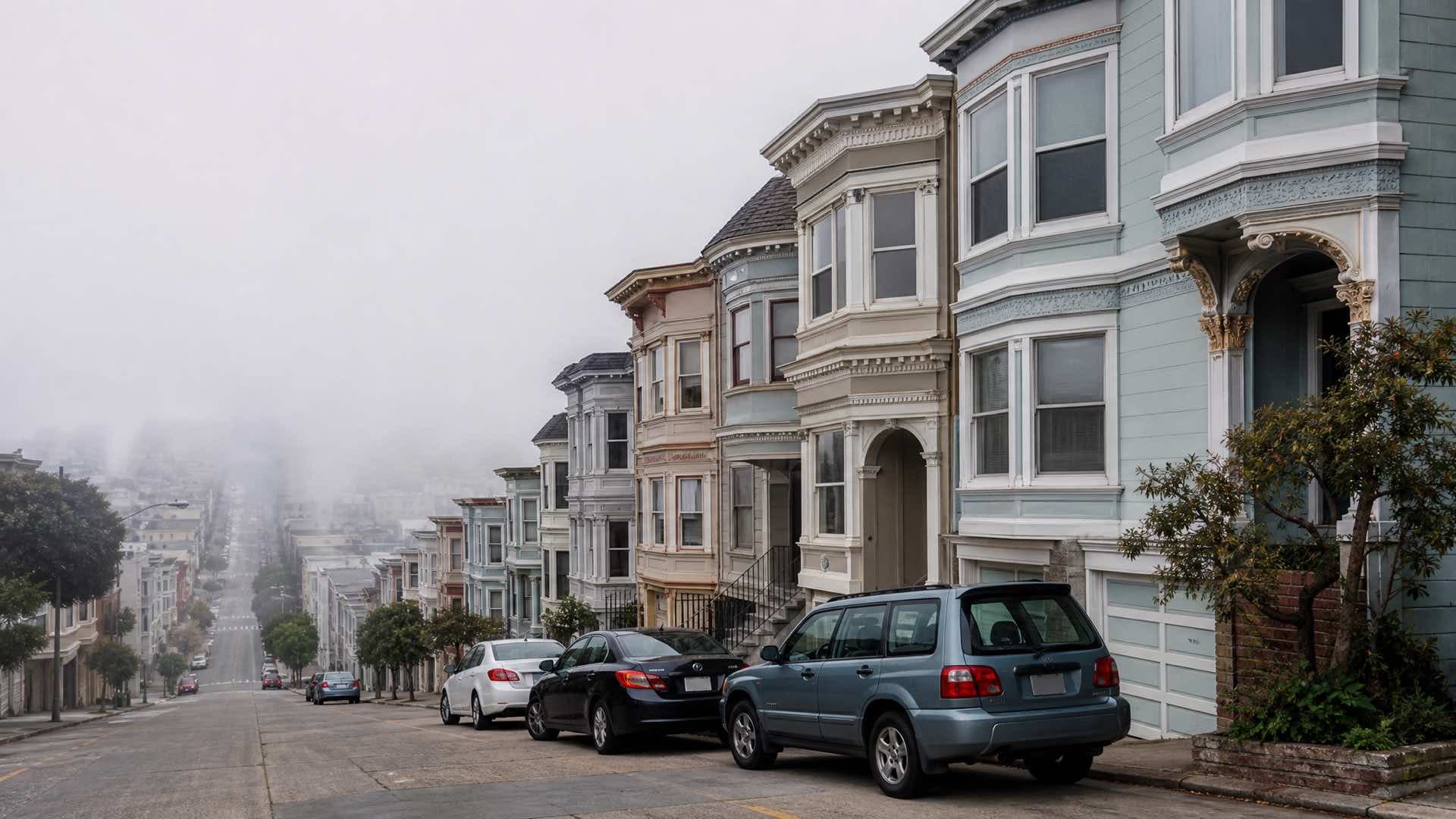 A steep San Francisco street of pastel Victorian houses with bay windows, low fog hiding the bottom of the hill